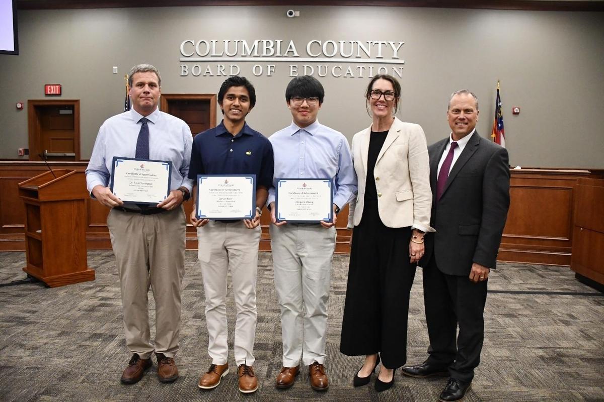 Five people lined up. Three are holding awards
