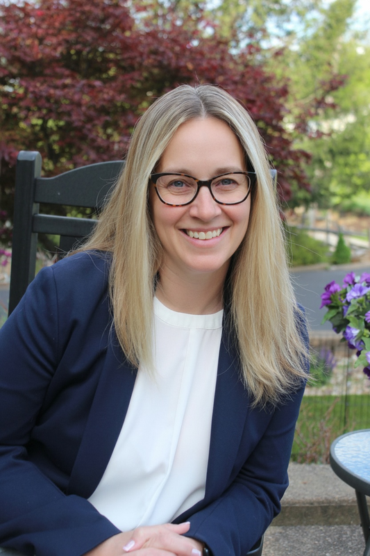 women with straight blonde hair and glasses smiles at camera in blazer