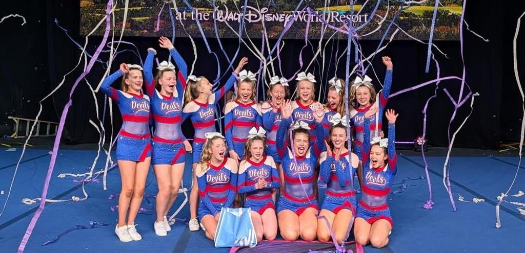 cheerleaders smiling and laughing in front of a sign that says Disney World with streamers floating through the air