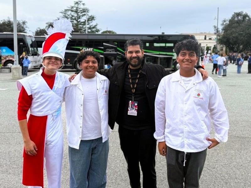 Three male students and their music director smile at the camera after their tournament of roses participation.