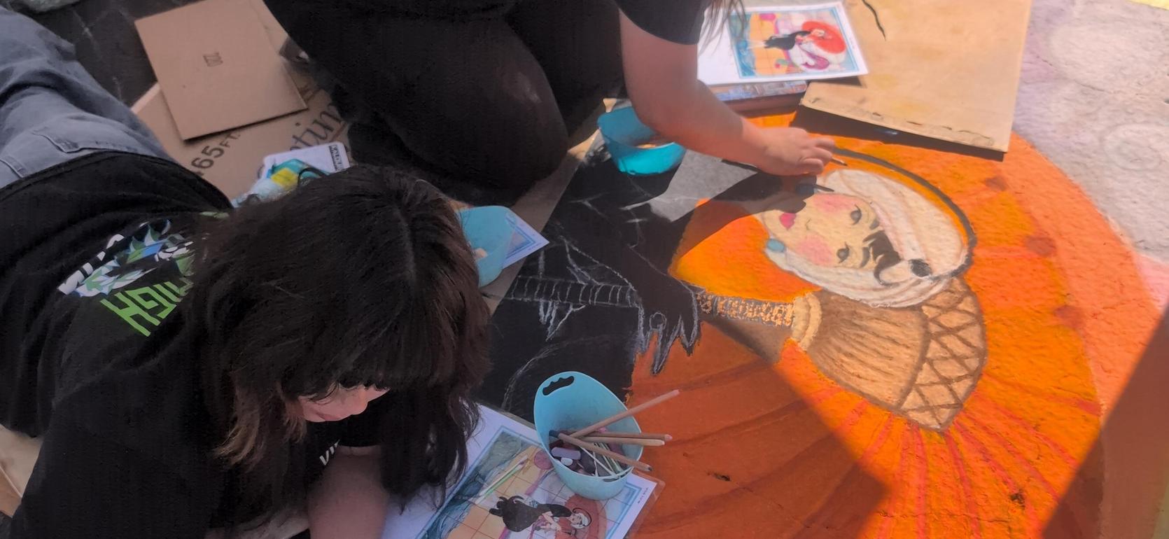 Two artists working on a detailed chalk drawing of a woman under an umbrella on pavement.