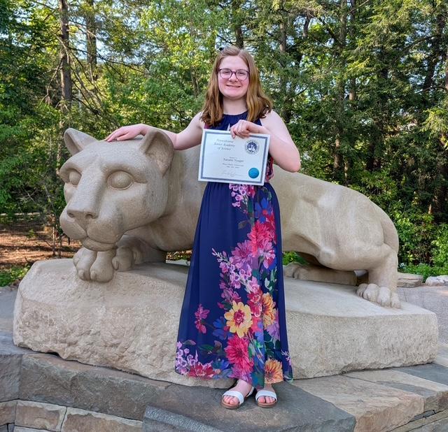 girl in blue dress holds 1st place certificate in front of nittany lion