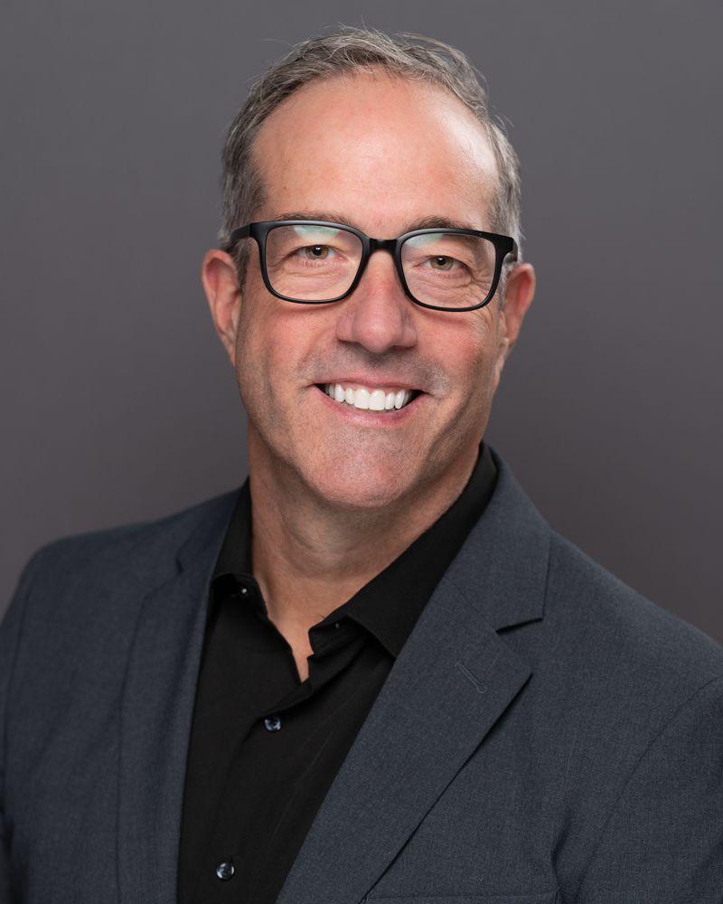 Smiling man in a suit against a gray background.