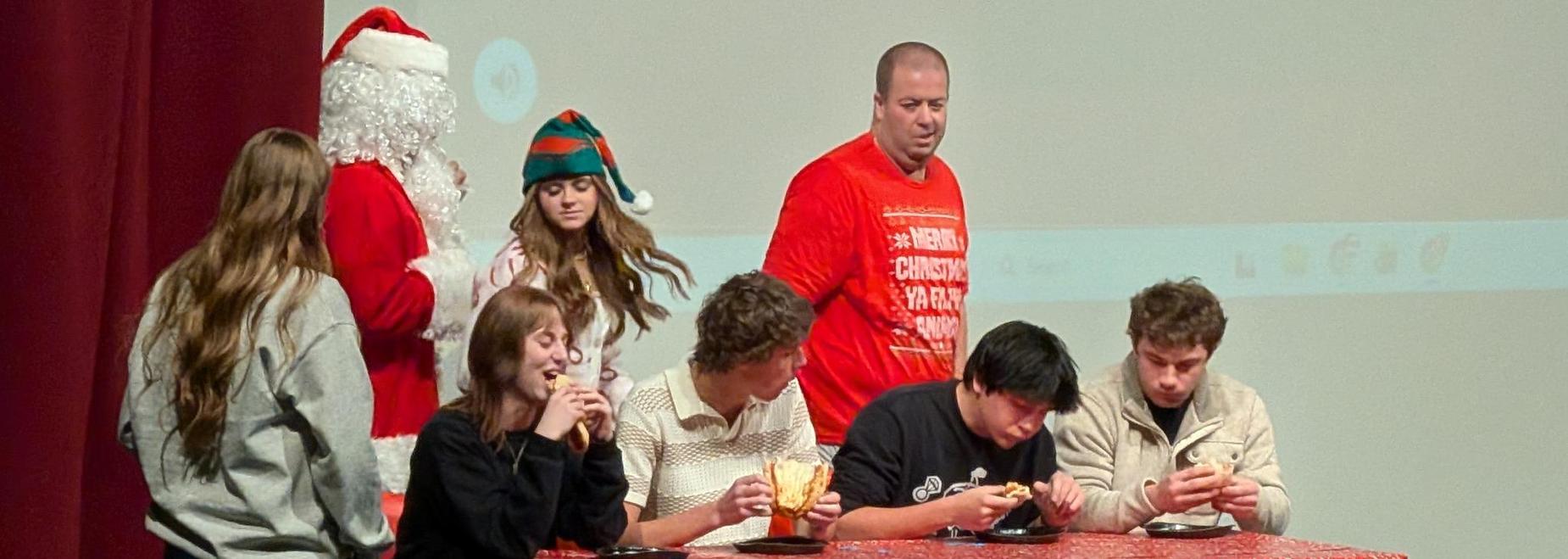 Students in festive costumes on stage with holiday treats.
