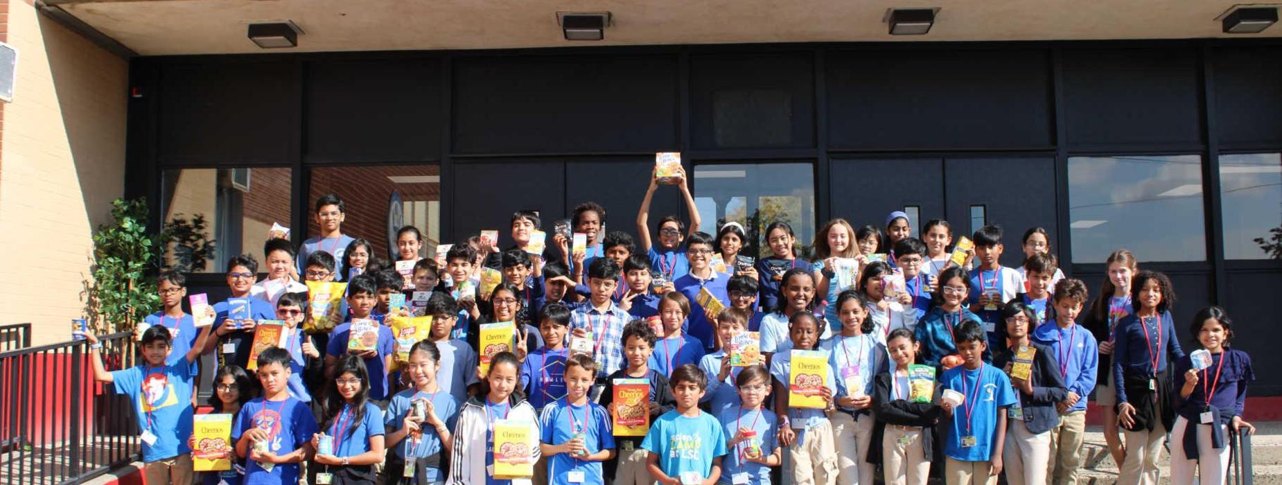 Large group of students in blue shirts holding various snacks outdoors.