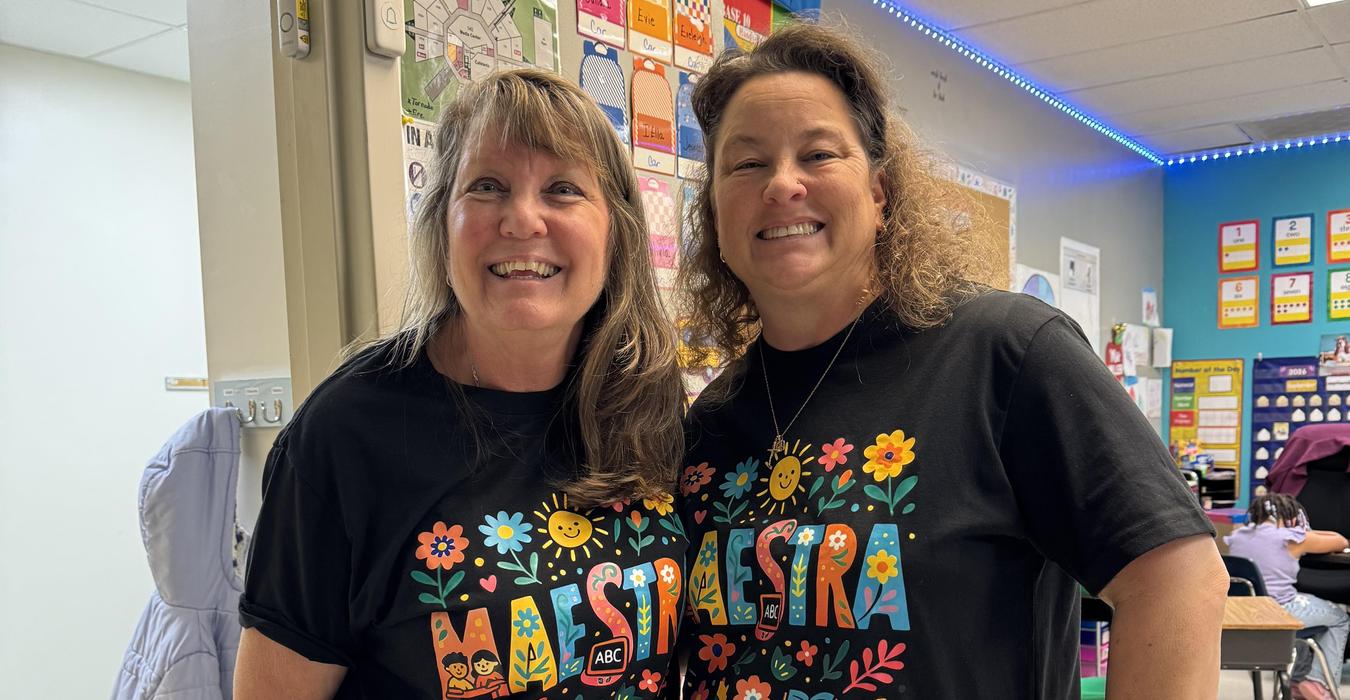 Two women in matching floral t-shirts smiling in a classroom setting.