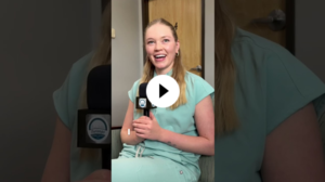 Person in light blue scrubs sitting indoors, holding a Durango School District-branded microphone and smiling during an interview.