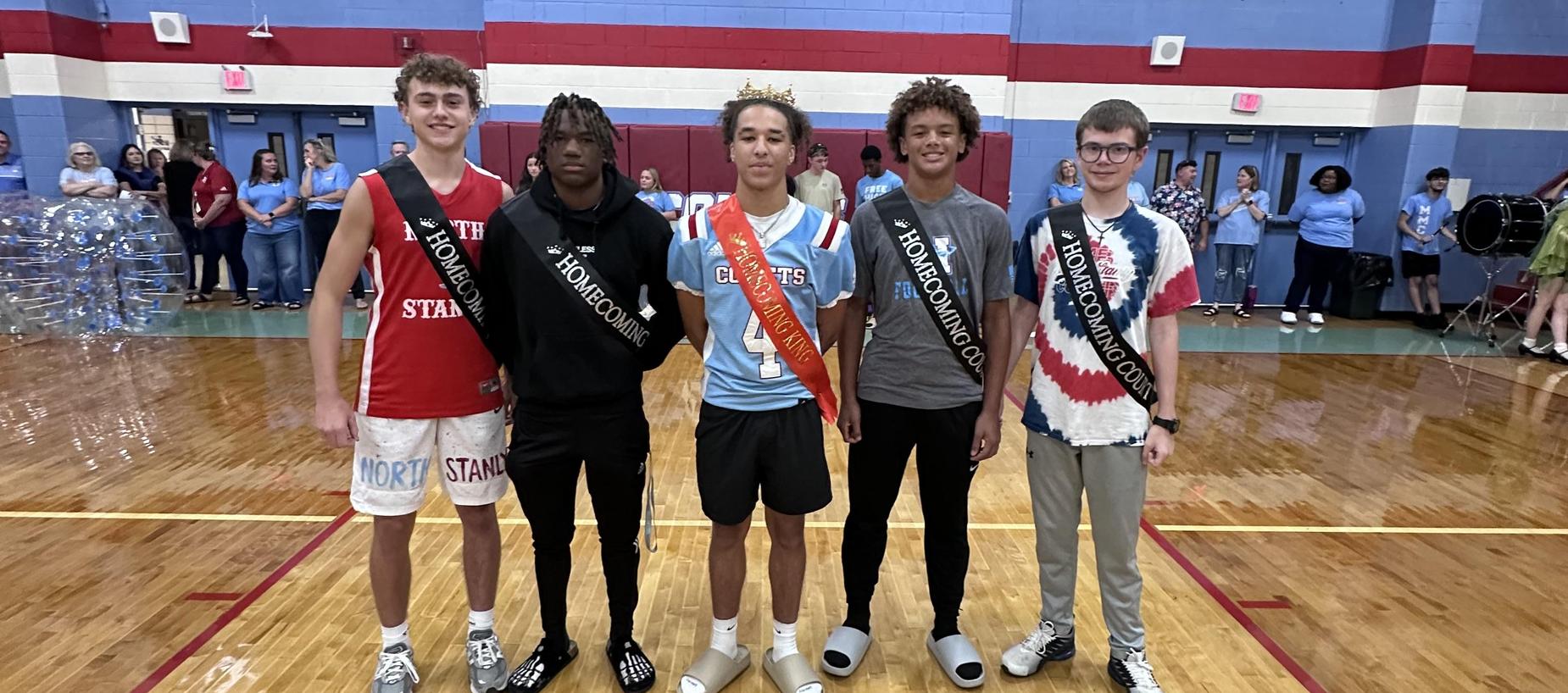 Five students in athletic wear celebrate Homecoming with sashes and crowns.