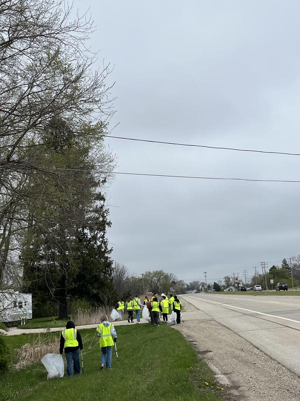 Volunteers in yellow vests cleaning up alongside a highway on a cloudy day.