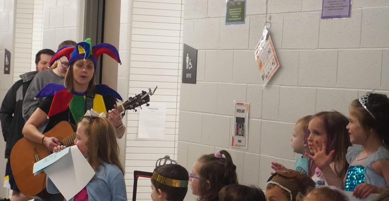 An ECC teacher dresses up as a court jester and sings songs with the students during the literacy ball.