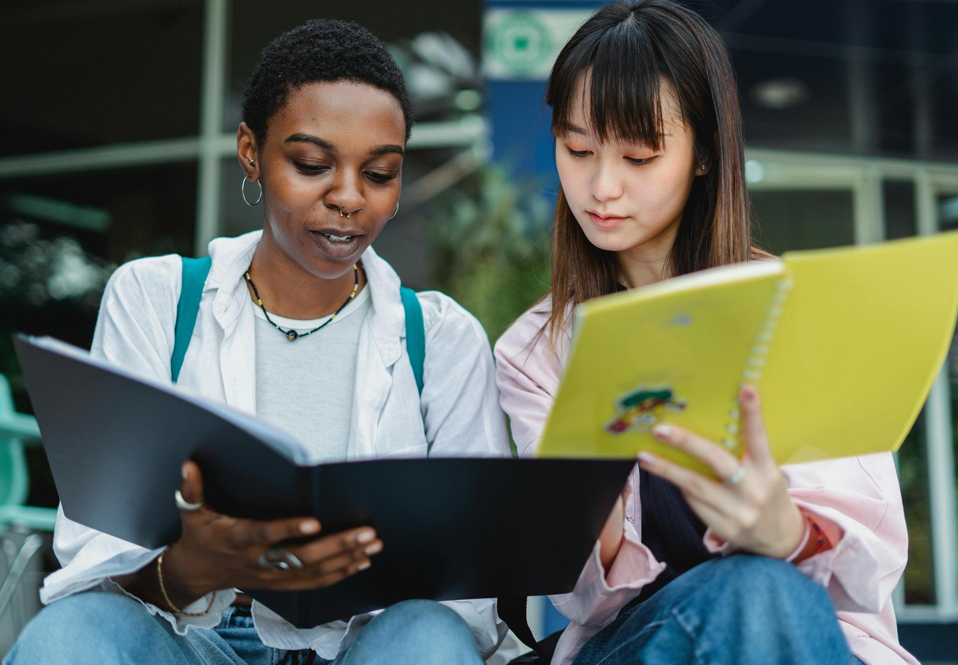 Two students reading and discussing study materials outdoors.