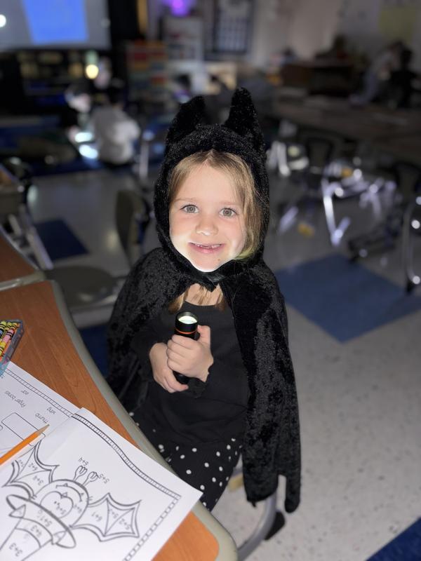 girl dressed as bat holding flashlight under chin