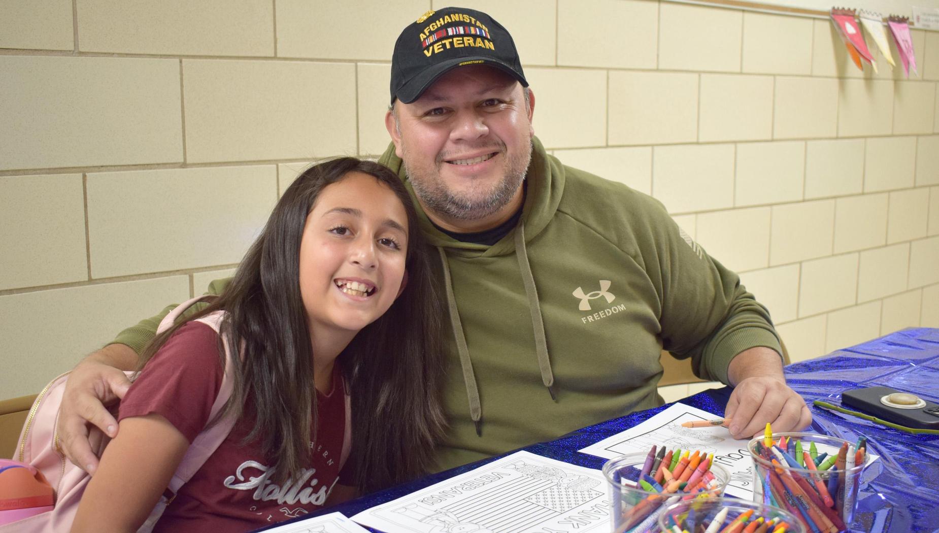 A girl and a man smiling together at a table with craft materials and a blue tablecloth.