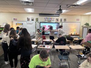 Students dancing and interacting in a lively classroom with art supplies and projects.