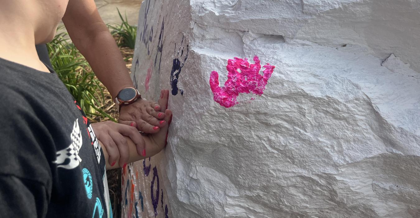 Two hands, one adult and one child, leaving colorful handprints on a rock.