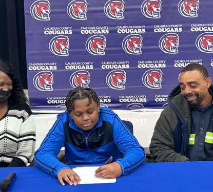 Student sitting at a table with his mother and father signing a reach scholarship form.