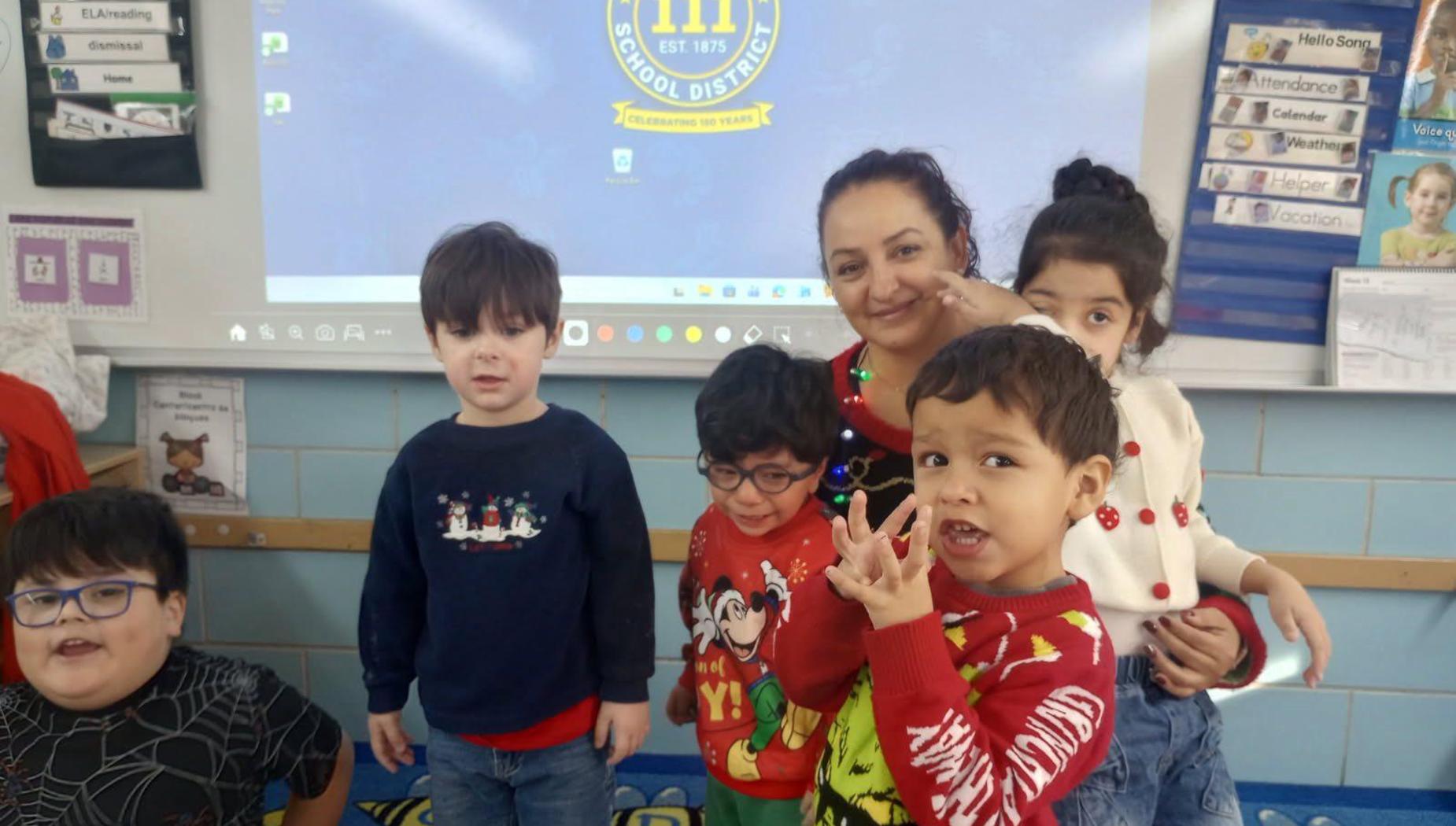 A teacher with several children around her, all wearing festive attire in a classroom environment.
