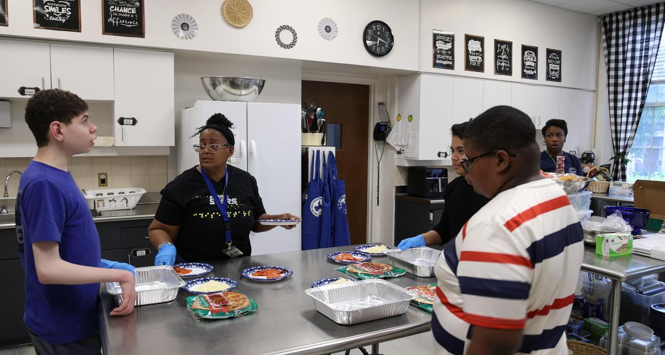 A group of people preparing food in a kitchen with plates and trays.