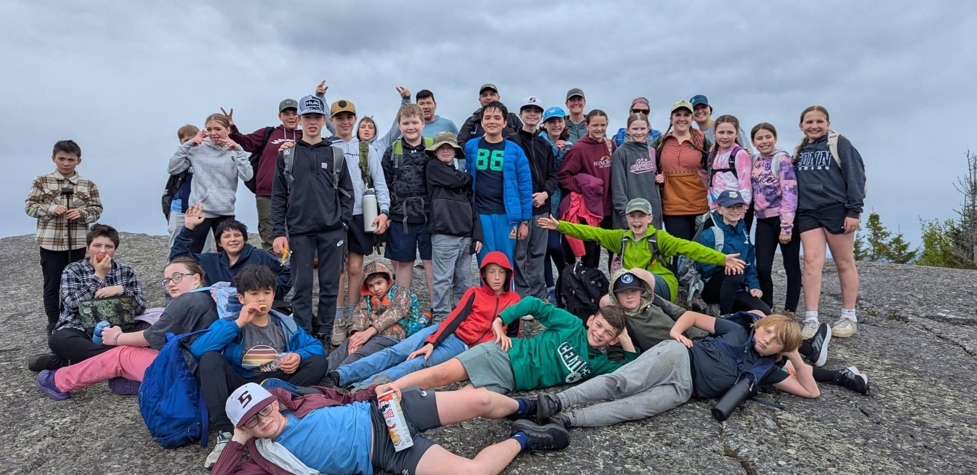 Group of students posing together on a rocky summit under cloudy skies.