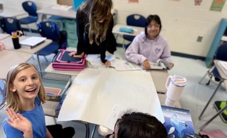 Students engaged in a classroom project with smiles and materials on their desks.