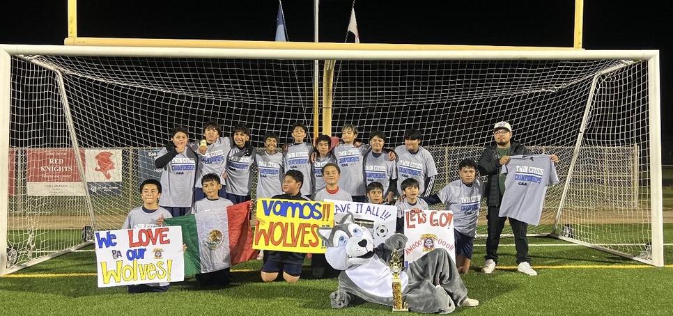 A youth soccer team celebrating a victory with banners and a mascot in front of a goal.