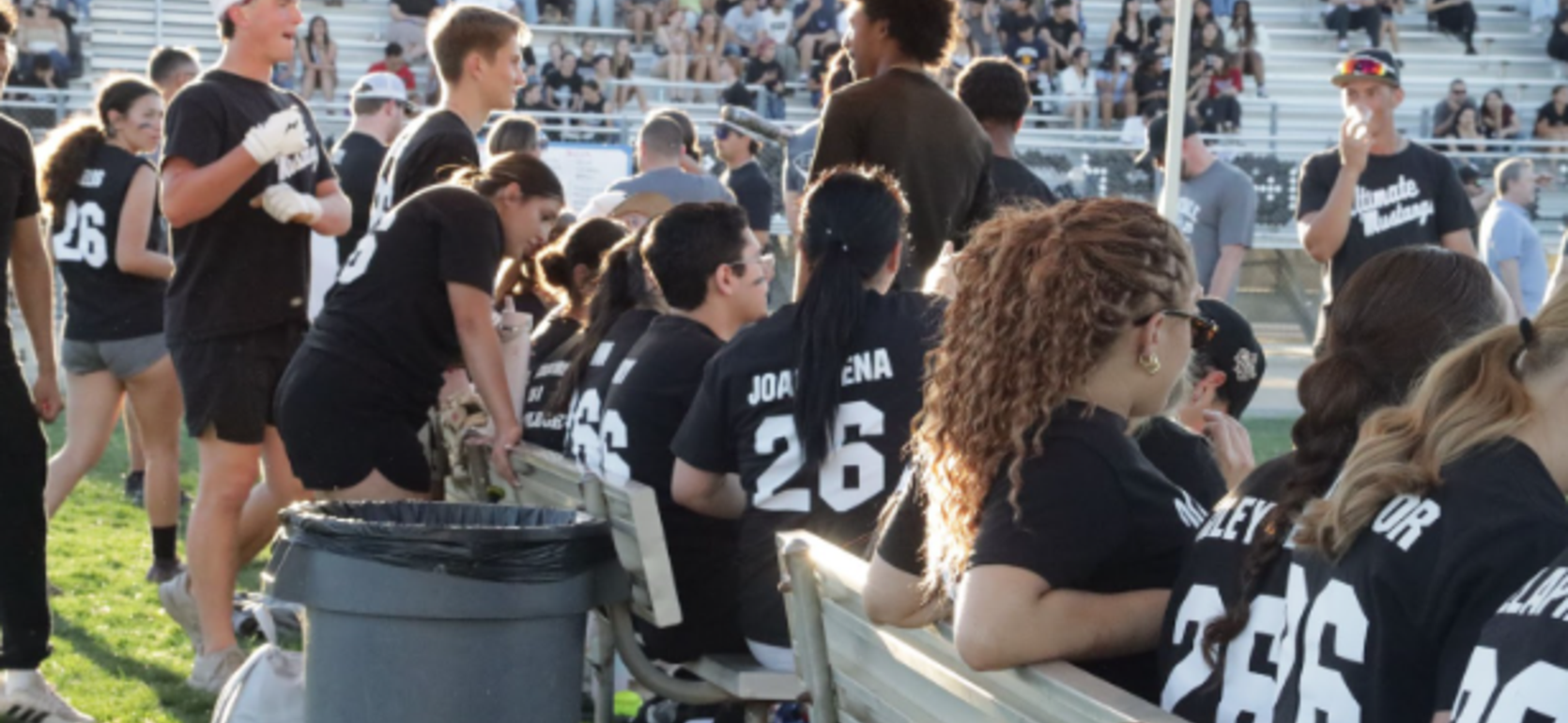 A group of people in matching shirts sitting on benches at an outdoor event.