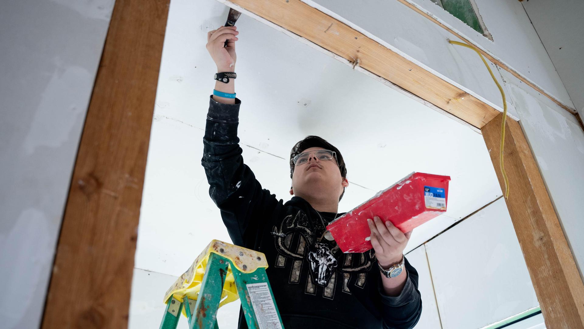 Person on a ladder painting a wall with a roller.