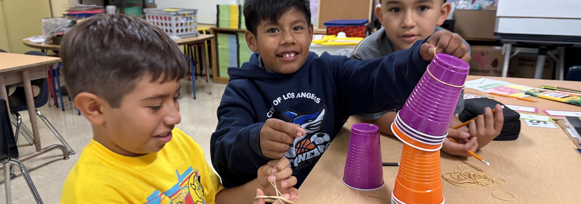 Three children are engaged in a hands-on activity with colorful cups and rubber bands.