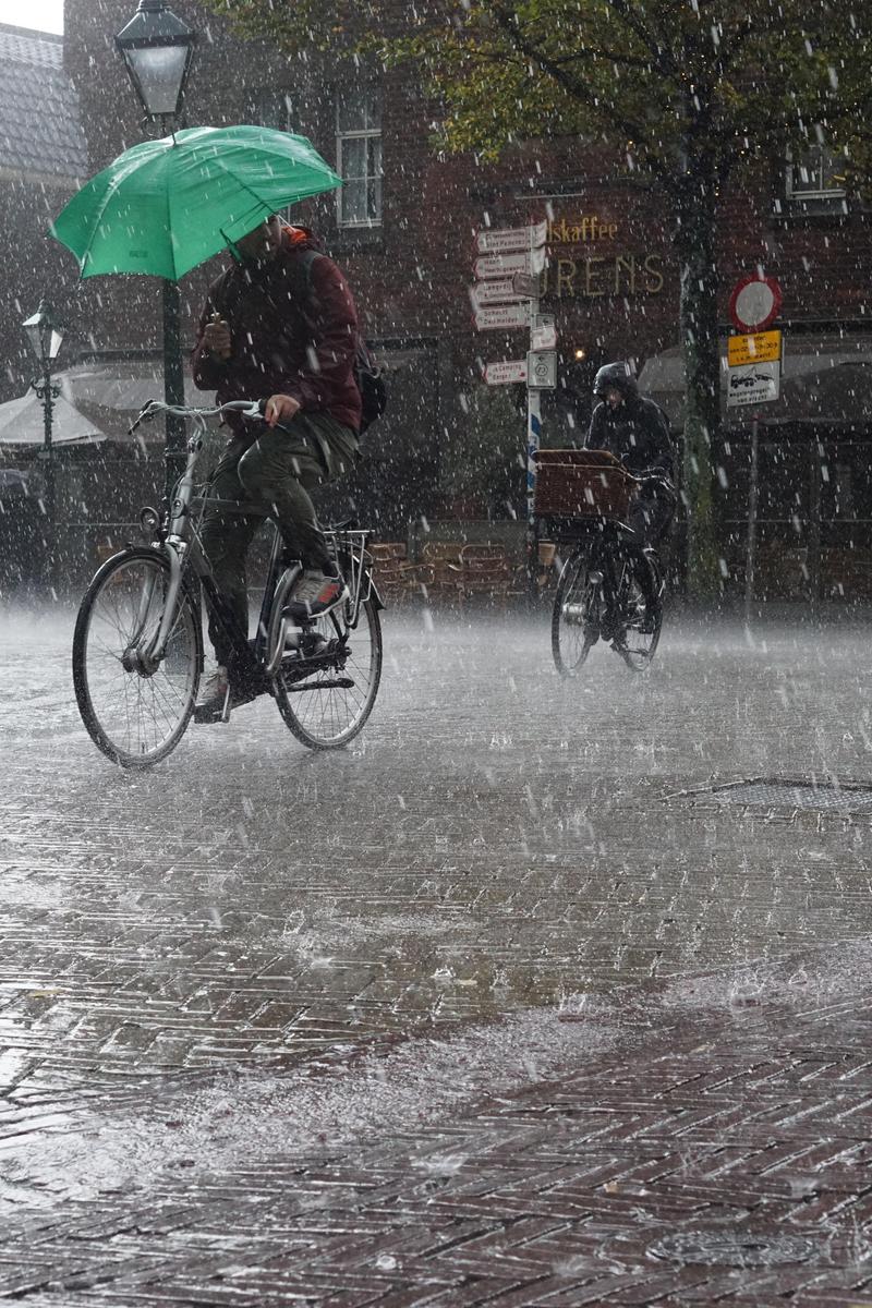 Cyclists riding in heavy rain, one with an umbrella and the other on a bike.