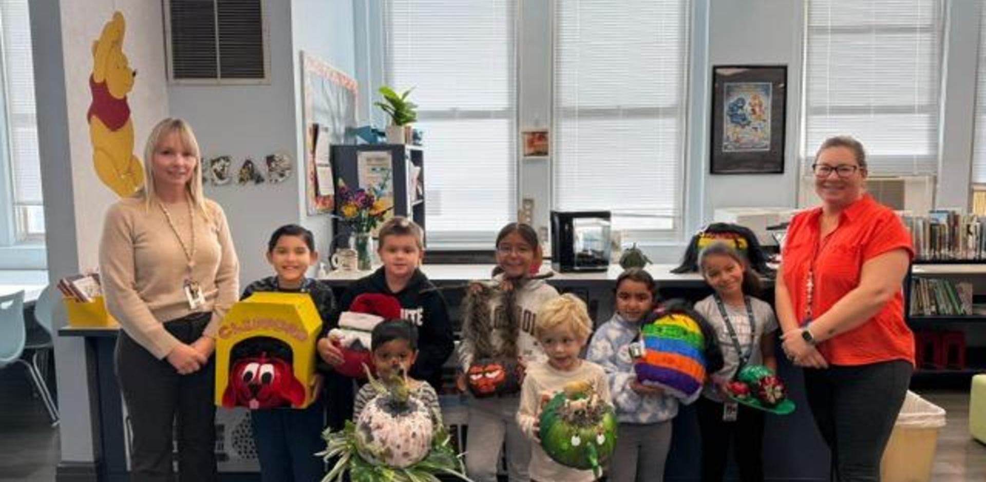 A group of children and adults displaying decorated hats in a classroom setting.