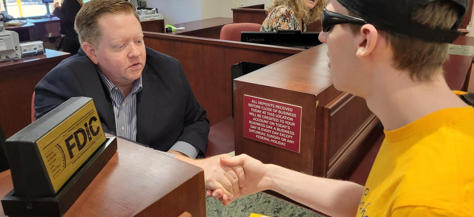 A banker shaking hands with a young man at a financial institution.