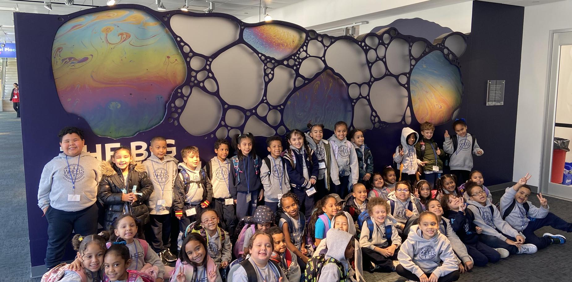 Group of children in matching outfits posing in front of a colorful art installation.