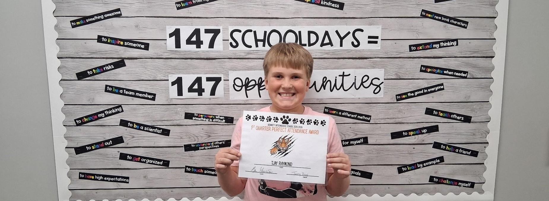 A smiling child holding a certificate in front of a motivational wall display.