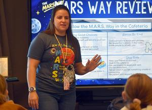 A teacher explaining a lesson with presentation slides in a classroom.