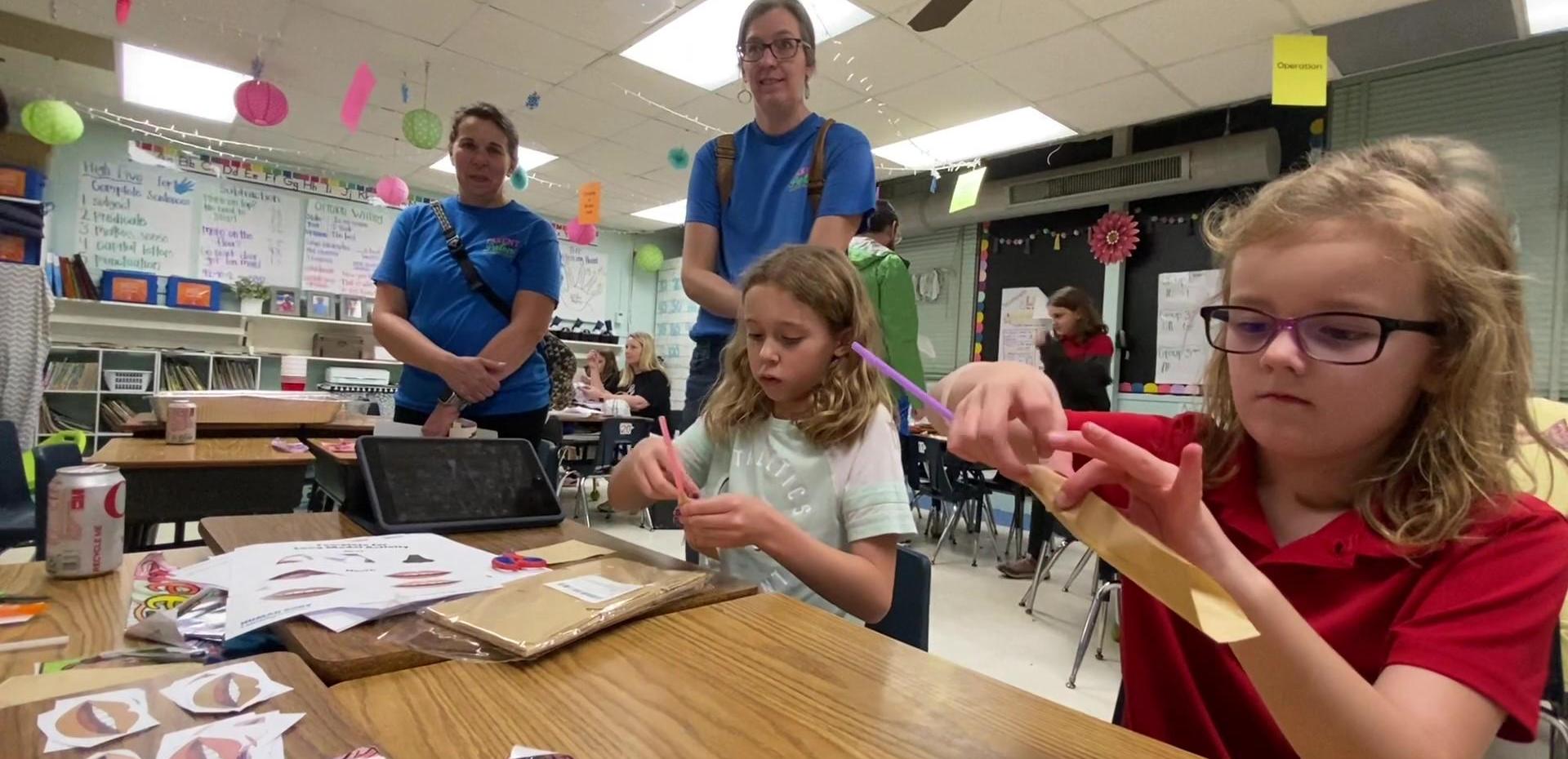 Students engaged in craft activities with teachers present in a classroom.