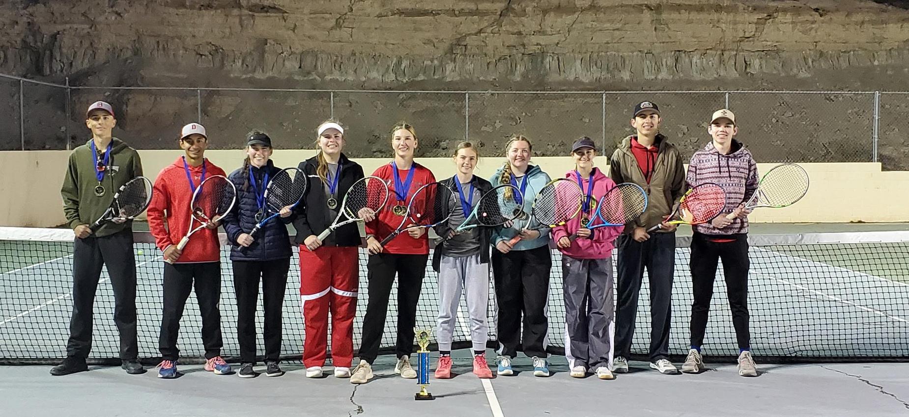 Group of tennis players holding trophies and medals on a court.