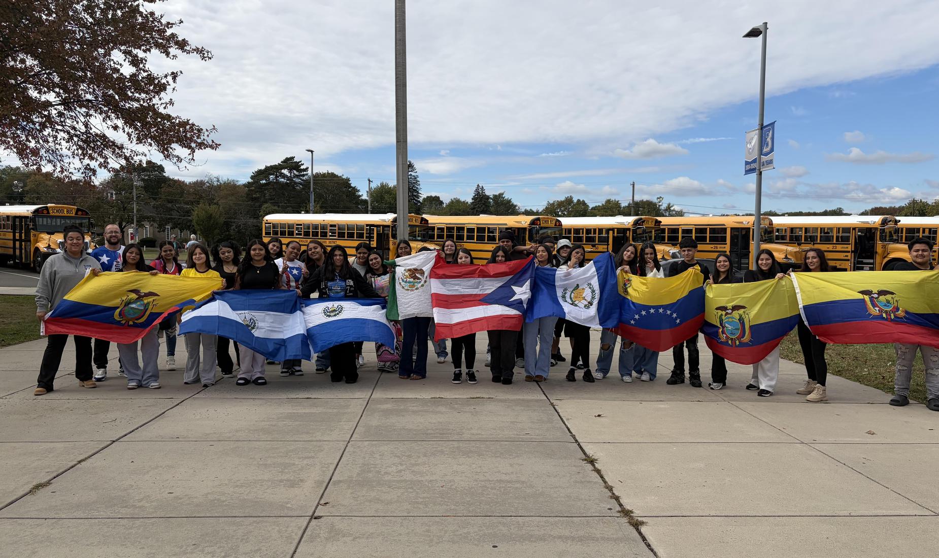 A diverse group of students holding flags from various countries outdoors.