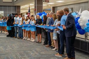 Group of students and staff hold the ribbon for the ribbon cutting.