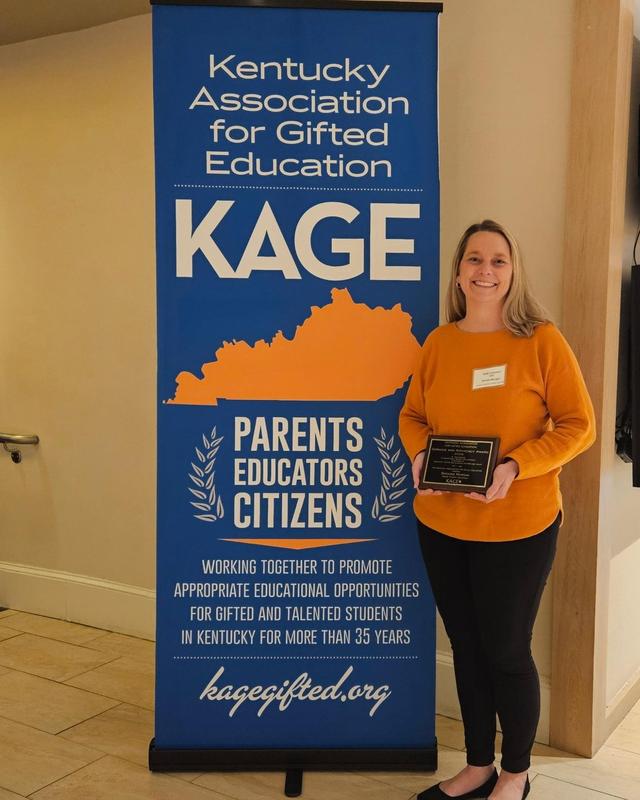 Brooke Morgan standing with KAGE Award in front of banner
