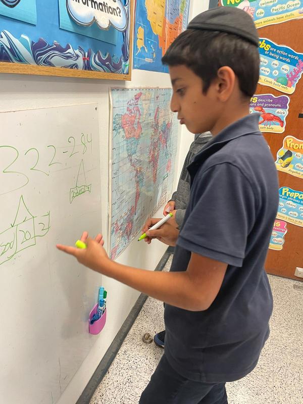A third grade student works to solve a math problem using a white board.