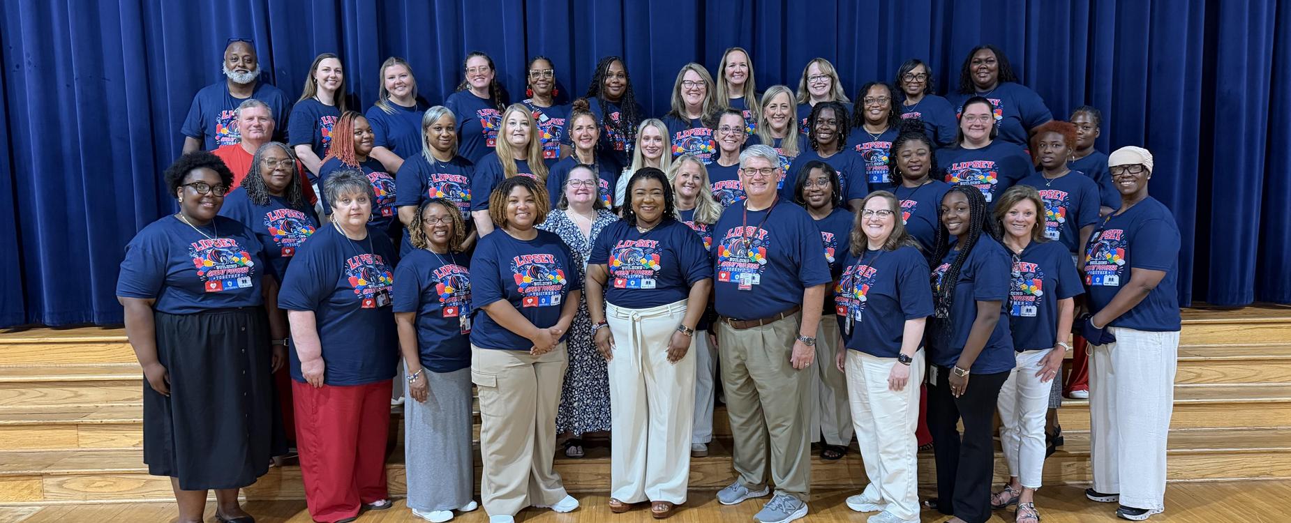 Group of diverse people in matching shirts posing together on stage.