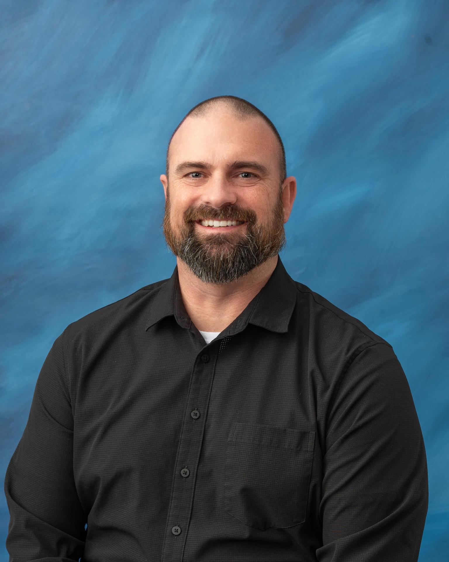  Photo of Mr. Justin Eckenrode with a black shirt in front of a blue background.