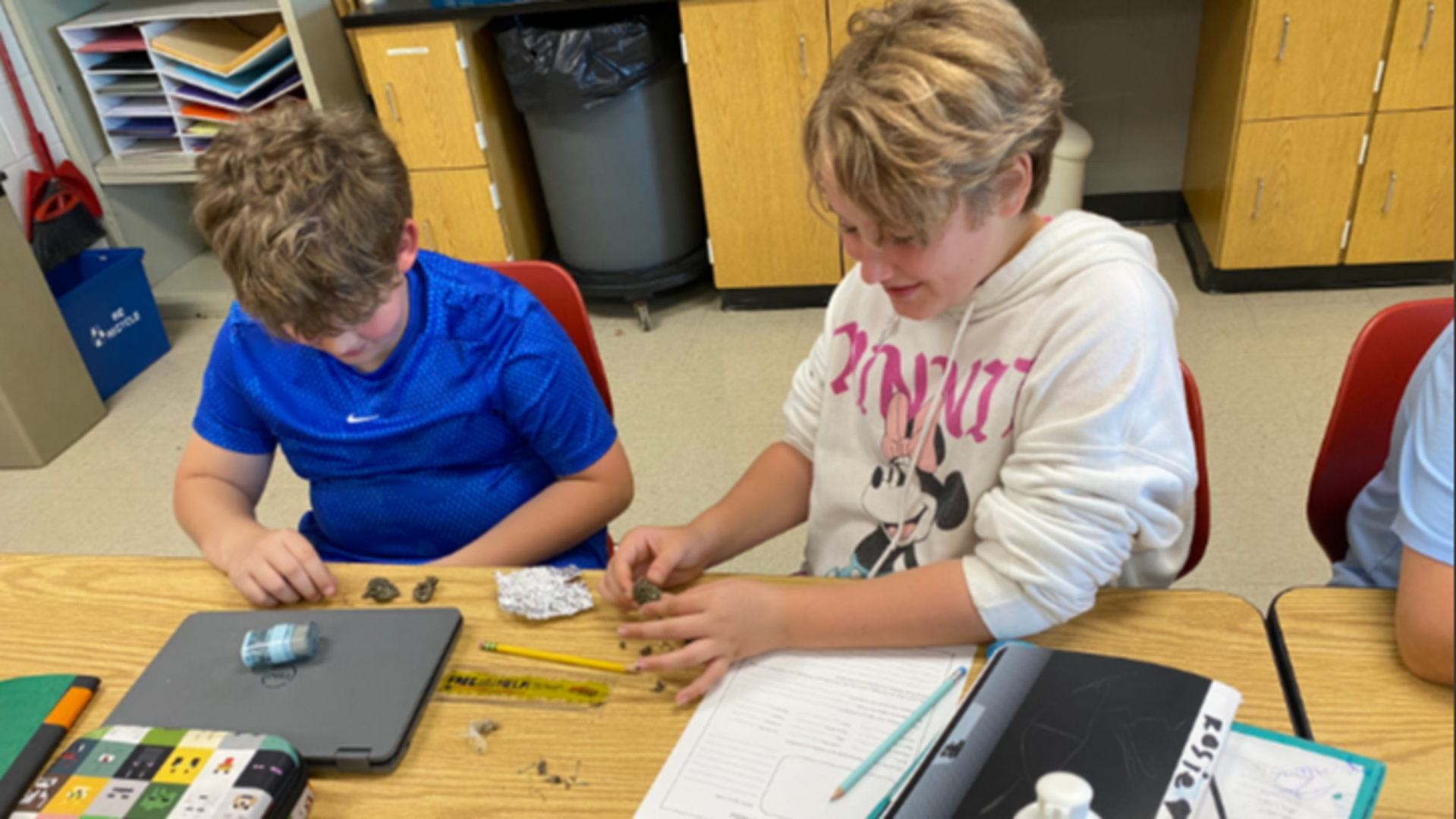 Two children engaged in crafting activities at a classroom table.