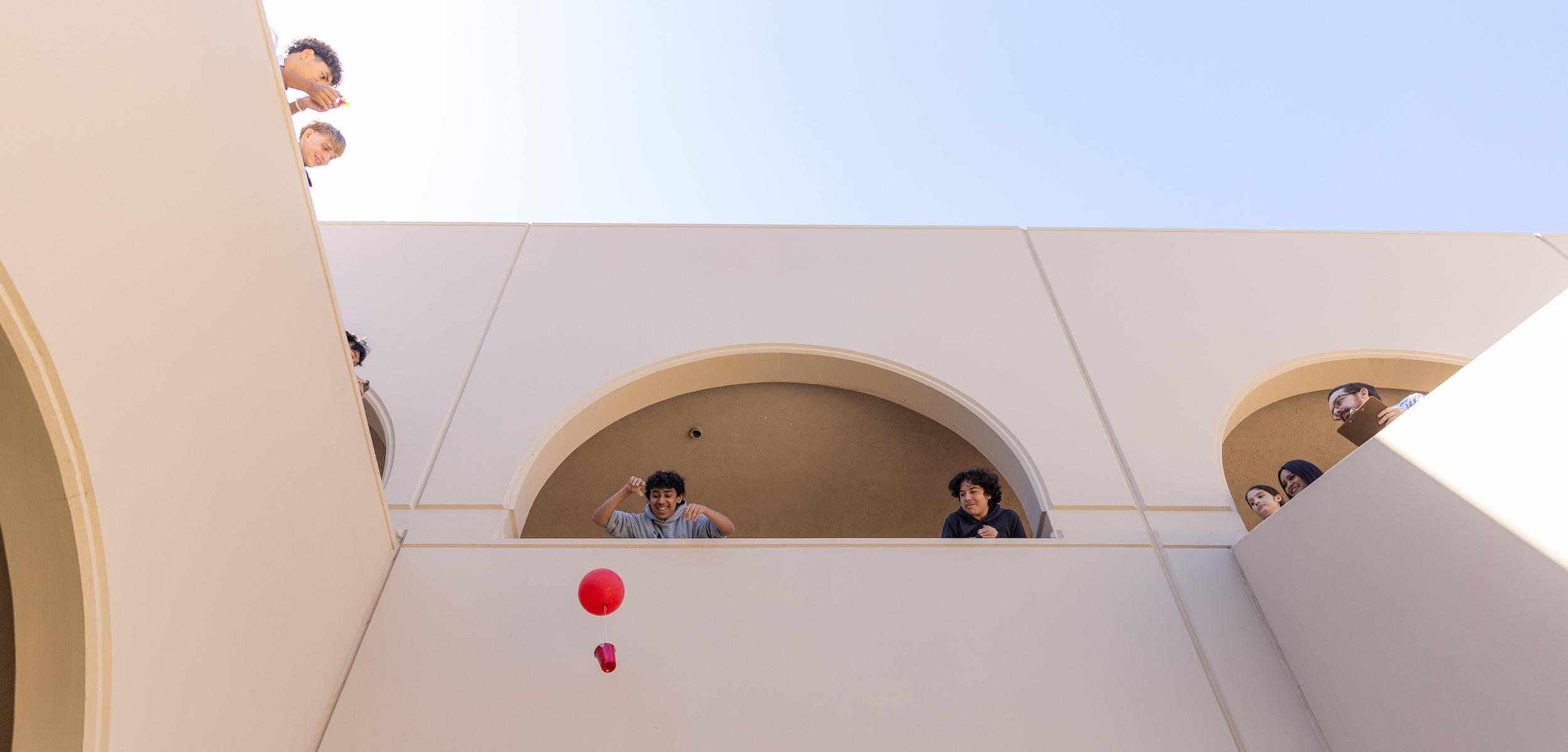 Students observe from above as a red ball is dropped from a balcony.