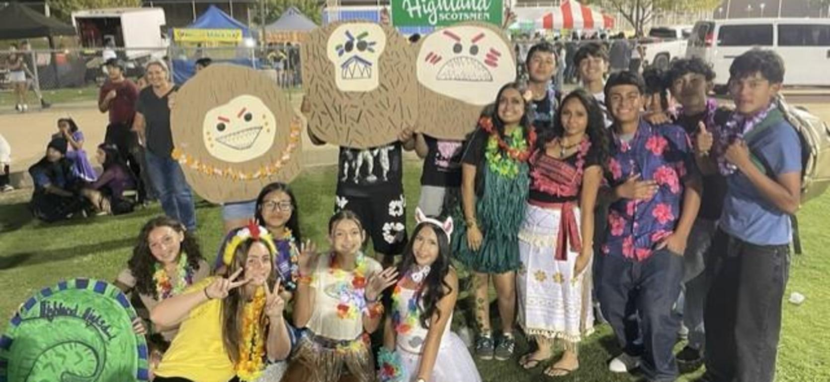 Group of students in festive clothing holding large themed cutouts at an outdoor event.