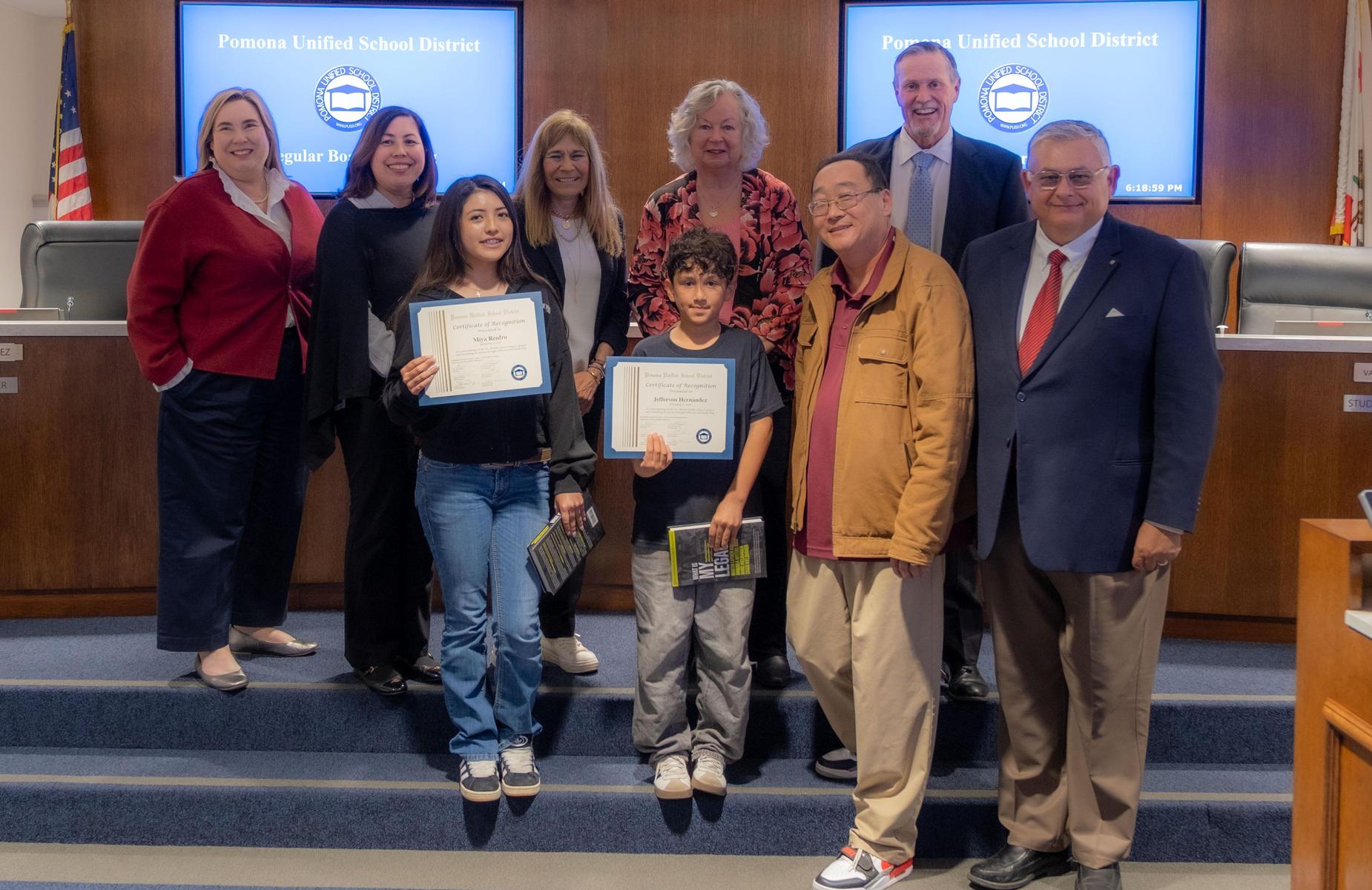 9 persons in school board room pose for photo with students