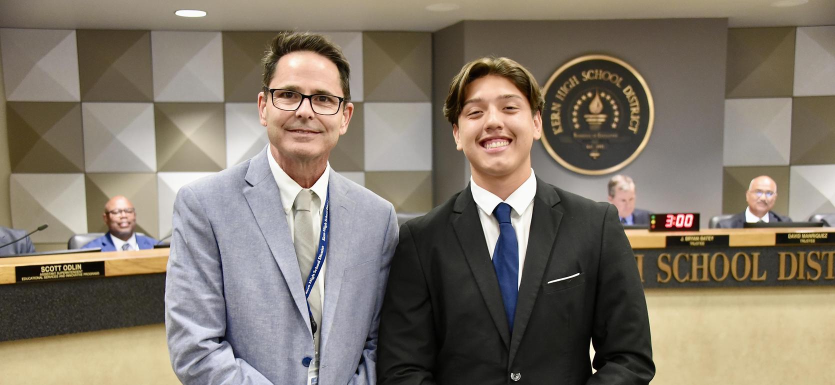 Two men posing together, smiling, in an official office setting.