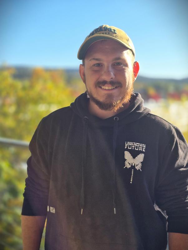 Man standing against a railing with a backdrop of trees