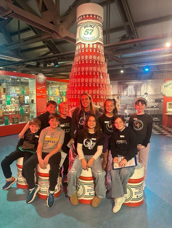 Image depicts a team of Quaker Valley students posing in front of a tower of Heinz ketchup bottles at the Heinz History Center.