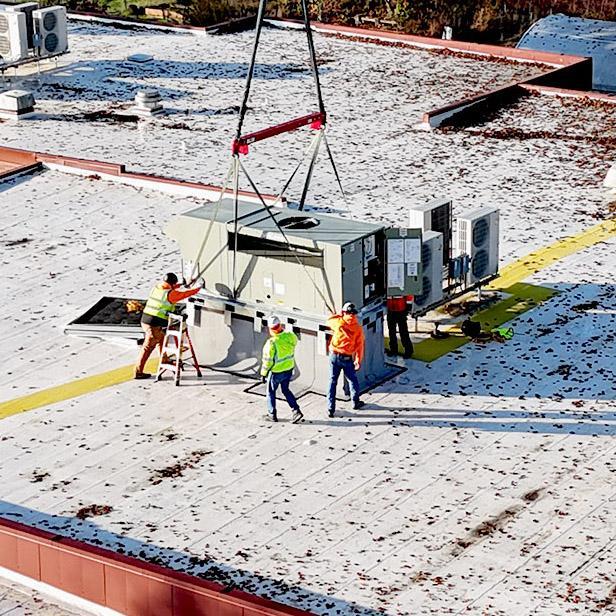 Crew members install rooftop HVAC unit